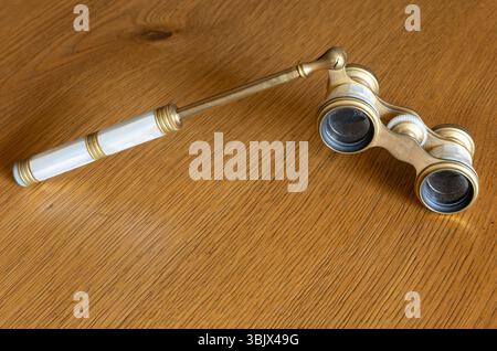Elegant vintage opera glasses with a mother-of-pearl handle rest on a wooden surface, evoking the charm of classical theater evenings. Stock Photo