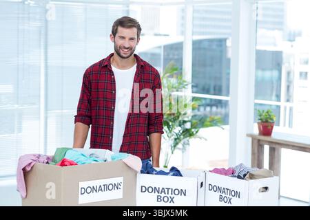 Mid-30s male volunteer standing behind donation boxes filled with clothing in community center room Stock Photo