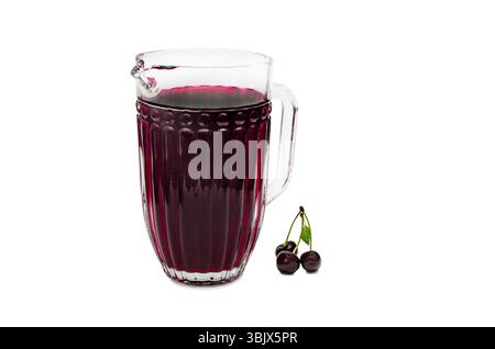 A clear glass pitcher filled with dark red cherry juice is placed on a white background. Three fresh cherries with stems and a green leaf are position Stock Photo