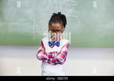 Schoolgirl is standing in front of green chalkboard with geometry diagrams and chalk dust on ledge Stock Photo
