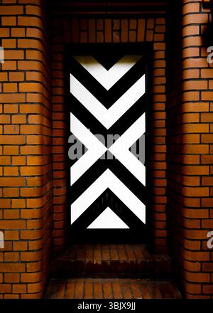A close-up shot of a brick wall with a door that has a black and white design on it. Stock Photo