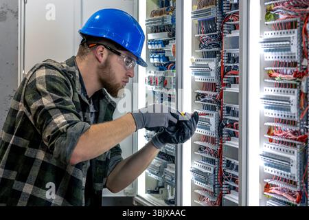 Electrician inspects switchboard. Wiring check. Screwdriver in hand. Stock Photo