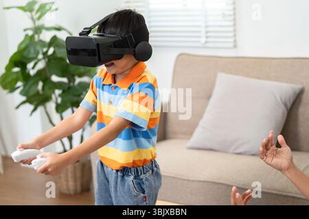 Child's Joy in Virtual Reality. Engaged boy experiencing VR gaming with father's encouragement. Stock Photo