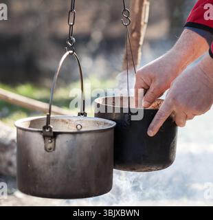 Man cooking in sooty old pots on bonfire Stock Photo