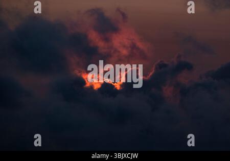 The setting sun lights up gathering clouds with an orange red glow over the ocean, Cornwall, England. Stock Photo
