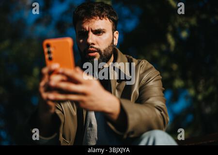 Man in leather jacket intensely focused on smart phone outdoors Stock Photo