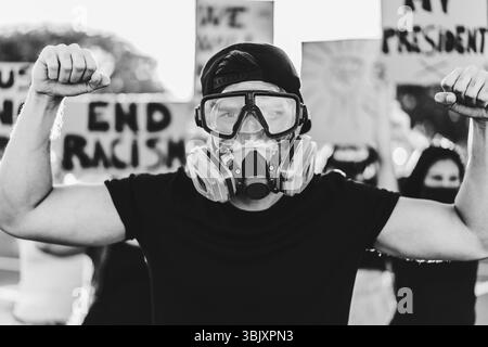 Multiracial immigrants protesting outdoor against government laws - Riot, demonstration and activist concept - Main focus on center man mask - Black a Stock Photo