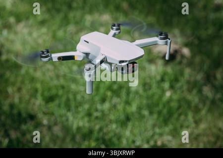 Small Flying Quadcopter Drone rotating propellers in flight mode with camera isometric side view outdoor on green summer background Stock Photo