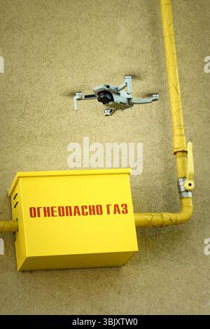 Drone in the air inspecting gas box and pipe, and text Flammable Gas on wall dangerous closeup yallow wall background Stock Photo