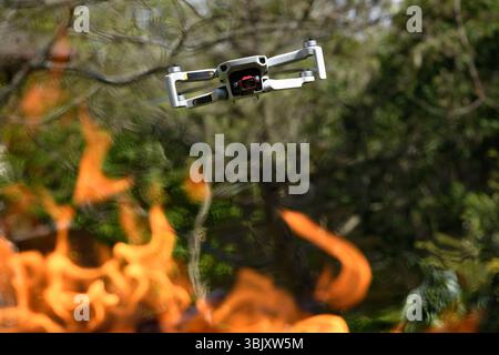 Flying drone Quadcopter with camera pointed at viewer outdoor in a fire in the foreground spurts of flame on forest background Stock Photo