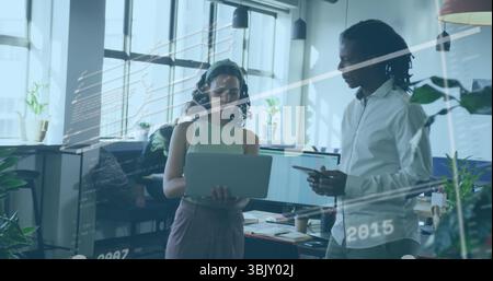 Collaborating developers reviewing code on laptop and tablet in open-plan office, with code overlay Stock Photo