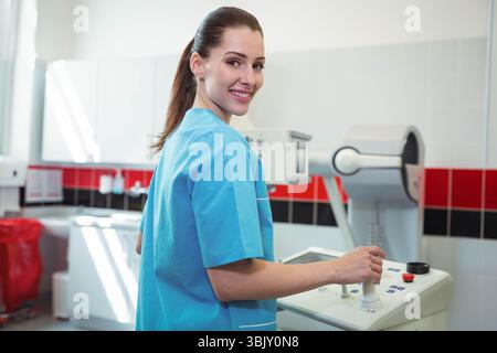 Woman adjusting controls on imaging console in radiology room with biohazard bin wearing scrubs Stock Photo