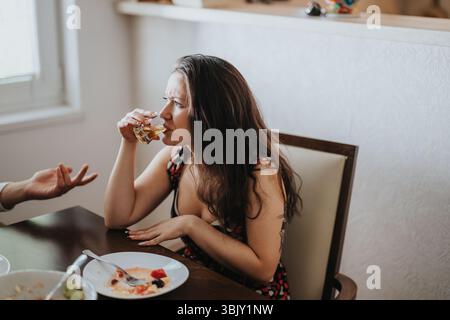 Woman drinking whiskey while talking at a dining table Stock Photo