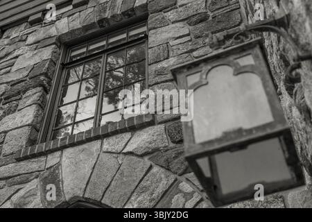 Black and white photo of stone wall, old window with reflections, vintage metal lantern, rustic texture, historic building detail. Stock Photo