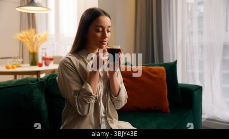 Happy relaxed peace dreamy woman calm female girl lady at home drinking coffee morning drink aroma black tea holding cup of beverage dreaming thinking Stock Photo
