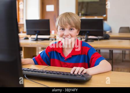 Preteen boy sitting at wooden desk in school computer lab using desktop computer and mouse Stock Photo
