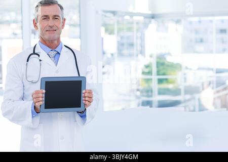 Physician wearing lab coat and stethoscope holding tablet by clinic windows overlooking city Stock Photo