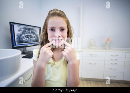 Child female patient pointing at lower teeth at dental clinic with computer monitor showing X-ray Stock Photo