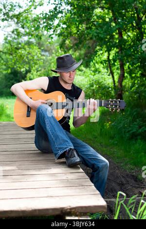 Man playing guitar in the woods on the bridge Stock Photo