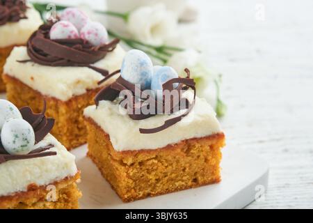 Easter carrot cake bars decorated with chocolate nest and chocolate candy eggs blossoming cherry or apple flowers on rustic ligh Stock Photo