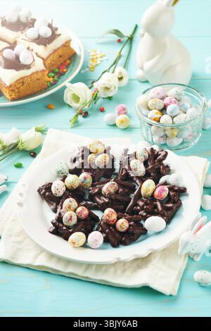 Easter chocolate nest cake with mini chocolate candy eggs with blossoming cherry or apple flowers on blue background table. Crea Stock Photo