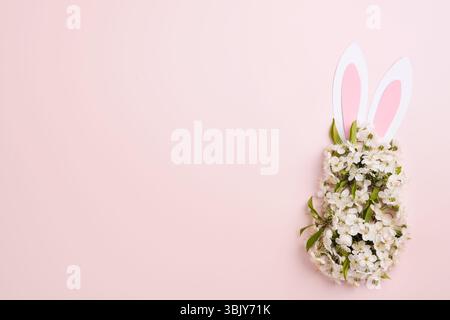 Happy Easter. Bunny rabbit ears made of pink paper and round bouquet of springs fresh cherry or apple blossoms on pink backgroun Stock Photo
