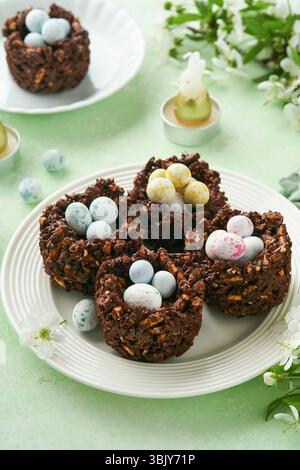 Easter chocolate nest cake with mini chocolate candy eggs with blossoming cherry or apple flowers on green background table. Cre Stock Photo