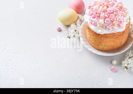 Traditional Easter sweet bread or cakes with white icing and sugar decor, colored eggs and cherry blossom tree branch over white Stock Photo