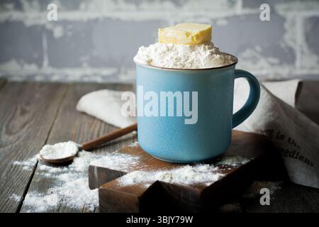 Ingredients and tools for homemade baking, flour and butter in a ceramic cup on an old wooden background. Selective focus Stock Photo