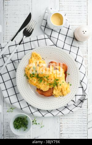 Scrambled Eggs. Fluffy and Buttery scrambled eggs on bread with microgreen radish and hollandaise sauce on white plate over whit Stock Photo