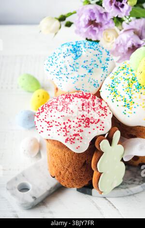 Traditional Easter sweet bread or cakes with white icing and sugar decor and quail eggs over white wooden table. Various Spring Stock Photo