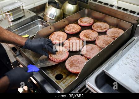 Chef cooking hamburgers on a hot professional griddle in a fast food restaurant kitchen Stock Photo