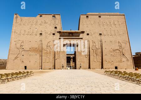EDFU, EGYPT – OCTOBER 26: The Temple of Horus, a well-preserved ancient Egyptian temple, stands under a clear blue sky. Rows of chairs are set up in the courtyard, awaiting visitors to explore the hieroglyphs and architecture. Stock Photo