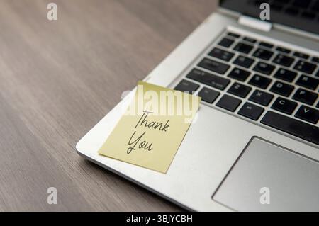 A sticky note with "Thank You" on the corner of a laptop. Gratitude, appreciation, recognition, and positive interaction in a modern workspace. Stock Photo