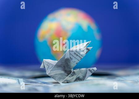 An origami bird folded from a US dollar bill and a globe. International financial transfers, remittances, and global money movement concept. Stock Photo