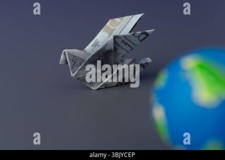 An origami bird folded from a US dollar bill and a globe. Global finance, international trade, and the worldwide movement of money. Stock Photo