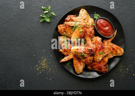 Chicken wings. Grilled or baked chicken wings with sesame seeds and ketchup or spicy tomato sauce on black plate on black or dar Stock Photo