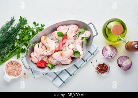 Raw chicken wings in a white bowl with spices and ingredients for cooking on light slate, stone or concrete background. Top view Stock Photo