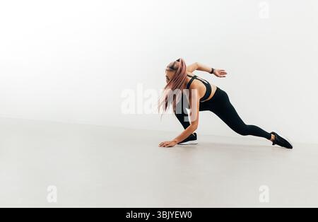 Young woman in sports clothes doing warming up jumps indoors. Athlete preparing for training. Stock Photo