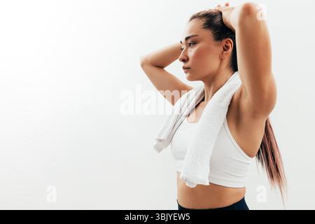 Portrait of an Asian woman relaxing during a workout. Tired sportswoman with white towel on neck. Stock Photo