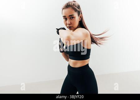 Woman doing kickboxing workout against a white wall. Female practicing punches. Stock Photo