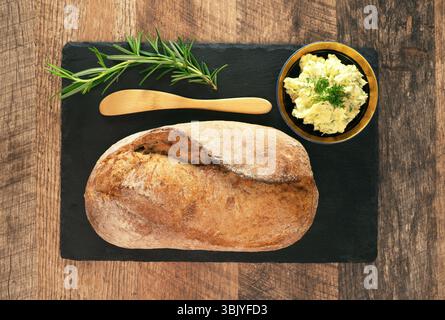 Freshly baked bread and rustic handmade herbs butter on the table. Stock Photo
