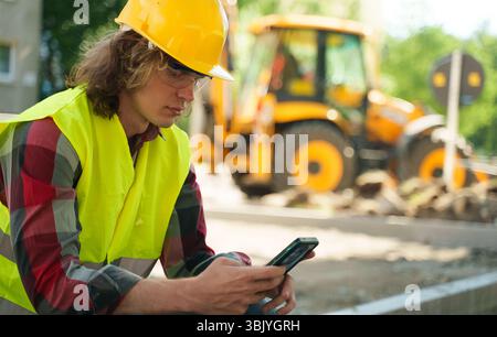 Male worker in hardhat and high vis jacket using smartphone. Stock Photo