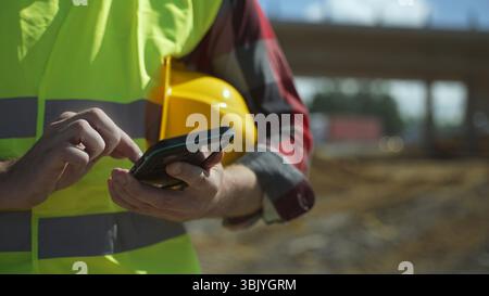 Builder with hard hat and high vis jacket using smartphone. Close-up. Stock Photo