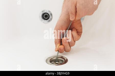 Plumber using drain snake to unclog bathtub. Stock Photo