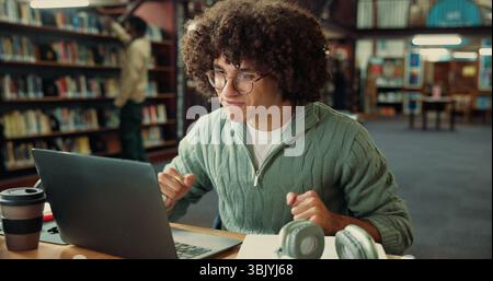 Student, excited and laptop with man in library for application approval, success and college. Scholarship award, university announcement and online Stock Photo
