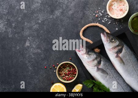 Sea Bass raw. Fresh sea fish bass with salt, pepper, parsley, olive oil and lemon on cutting board on dark concrete rustic backg Stock Photo