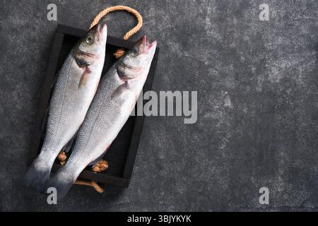 Sea Bass raw. Fresh sea fish bass with salt, pepper, parsley, olive oil and lemon on cutting board on dark concrete rustic backg Stock Photo