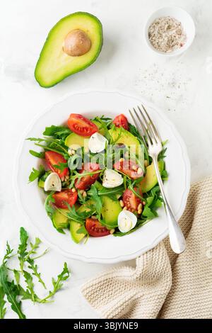 Fresh salad from arugula, tomato, avocado, olive oil, nuts and quail eggs on a light stone background. Selective focus Stock Photo