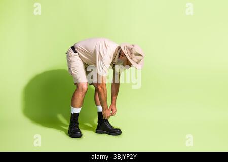 Elderly bearded man in safari outfit tying his boots, preparing for an adventurous expedition in the African wilderness. Stock Photo